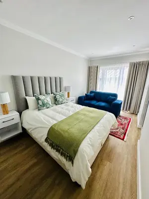 a bedroom with a large bed and a blue chair at Spacious Family Friendly Richwood in Cape Town