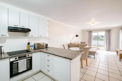 a kitchen with white cabinets and a living room at Belina - Century On Lake Moorings in Cape Town