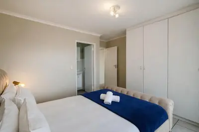 a white bed with a white cross on a blue blanket at Belina - Century On Lake Moorings in Cape Town