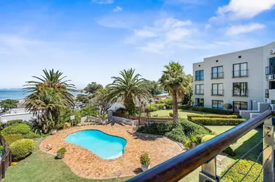 an apartment with a pool and palm trees and a building at Gordons Village View in Cape Town
