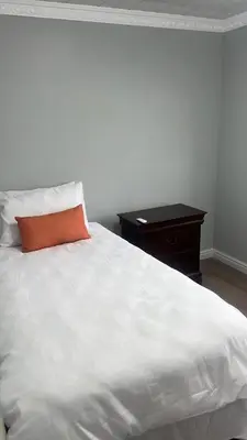 a white bed with an orange pillow and a table at Oryx guest house in Oakdale