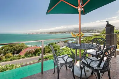 a table and chairs on a balcony with a view of the ocean at 18 On Kloof Guest House in Gordonʼs Bay