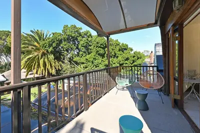 a balcony with chairs and tables and trees at Mawethu on Mead Guesthome with Covered pool and Garden in Cape Town