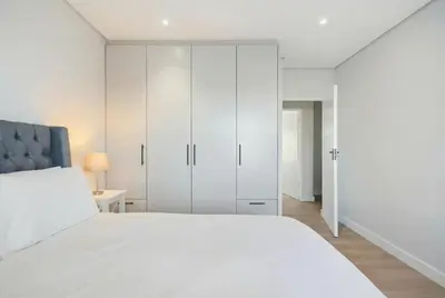 a white bedroom with a large bed and white cabinets at Cape Signature Villa in Cape Town