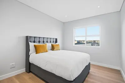 a white bedroom with a large bed with yellow pillows at Cape Signature Villa in Cape Town