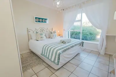 a white bedroom with a bed and a window at Seabreeze in Hermanus