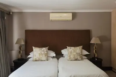 a bedroom with two beds with white sheets and two lamps at Whale Away Guest House in Hermanus