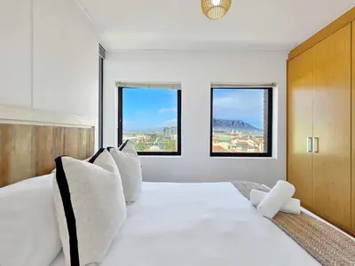 a white bedroom with a large white bed with windows at Sea, Canal & Mountain View, Rooftop Jacuzzi & BBQ in Cape Town