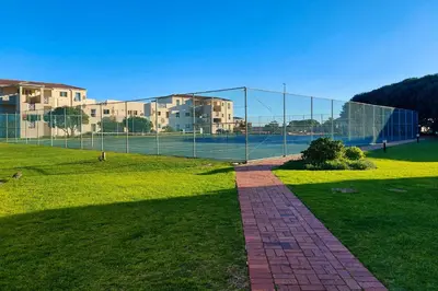 a chain link fence with a tennis court in a field at Nostalgie - Hermanus Beach Club in Hermanus