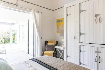 a bedroom with a bed and a chair and a sliding door at The Bay Cottage in Pringle Bay