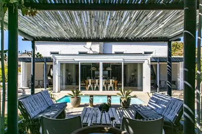 a patio with a table and chairs and a pool at The Bay Cottage in Pringle Bay