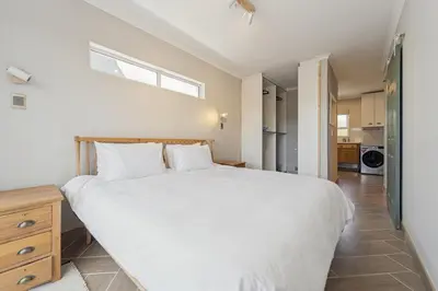 a bedroom with a large white bed and a kitchen at Lloyd's Corner in Cape Town