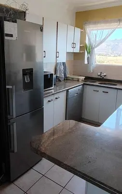 a kitchen with a stainless steel refrigerator and white cabinets at Windy Corner Luxury Apartment in Gordonʼs Bay