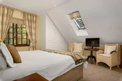 a bedroom with a bed and two chairs and a television at Gable Manor by Neighbourgood in Franschhoek