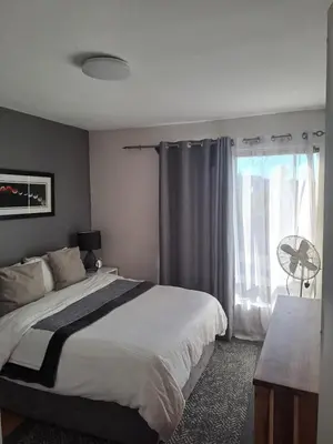 a bedroom with a bed and a window with a fan at Central 3rd Floor Durbanville Apartment in Durbanville