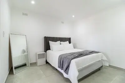 a white bedroom with a bed and a mirror at Flatlet on Circle in Cape Town