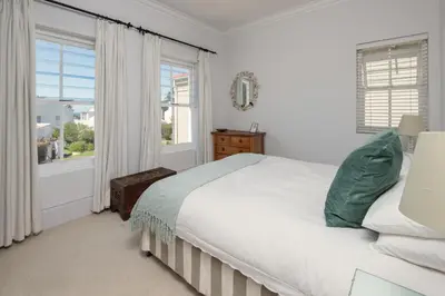 a white bedroom with a bed and two windows at Fir Close 3 bedroom in Hermanus