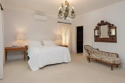 a white bedroom with a bed and a chair at Fir Close 3 bedroom in Hermanus