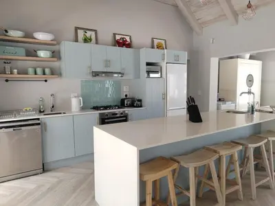 a kitchen with white cabinets and a counter with stools at Taylah's Hideaway in Bettyʼs Bay