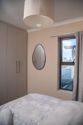 a bedroom with a bed and a mirror and a window at Cape on Viola in Cape Town