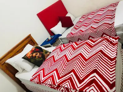 a bed with a red and white comforter at Annika`s dormitory in claremont in Cape Town