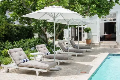 a group of lounge chairs and an umbrella next to a pool at River Manor Boutique Hotel by The Living Journey Collection in Stellenbosch