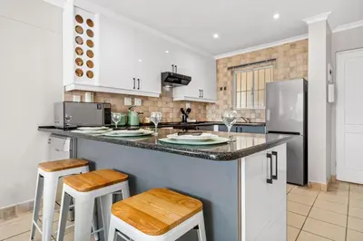 a kitchen with a counter with stools and a refrigerator at Coral Grove in Cape Town