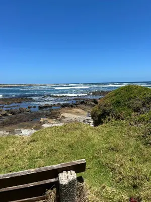 a wooden bench sitting on the side of a beach at Logans place in Hermanus