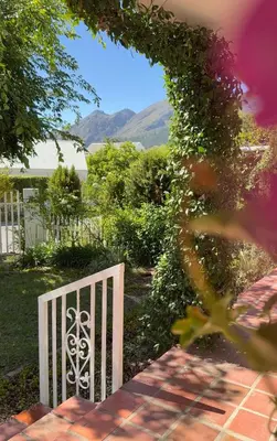 a white gate in a garden with mountains in the background at Crescent House in Franschhoek