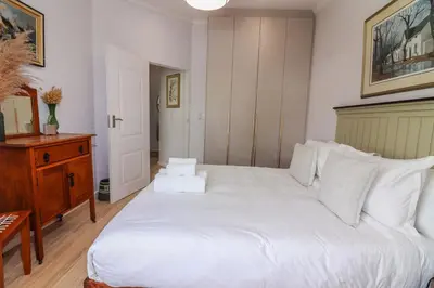 a bedroom with a large white bed and a wooden dresser at Blou Huis in Hermanus