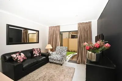 a living room with a black couch and a chair at Velvet & Bloom Cottage in Durbanville in Oakdale