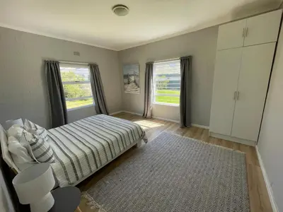 a bedroom with a bed and two windows and a rug at Silversands Serenity in Bettyʼs Bay