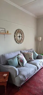 a couch in a living room with a clock on the wall at Bot River Farm Cottage in Botrivier