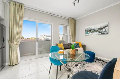 a living room with a glass table and blue chairs at The Orion 16 in Table View