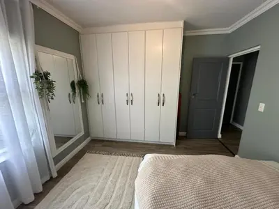 a bedroom with white cabinets and a bed and a mirror at Chasing Sunsets sea and mountain views in Hermanus
