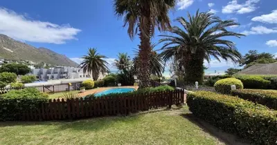 a fence with palm trees and a swimming pool at Beachside Bliss Gordons Bay in Gordonʼs Bay