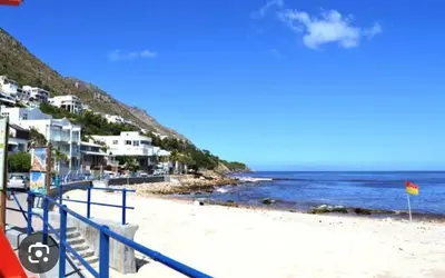 a beach with a blue railing and the ocean at Beachside Bliss Gordons Bay in Gordonʼs Bay