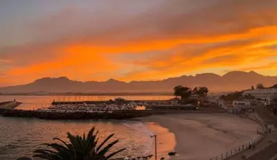 a sunset over a beach and the ocean at Beachside Bliss Gordons Bay in Gordonʼs Bay