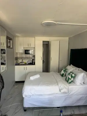 a bedroom with a large white bed and a kitchen at Legacy lodge in Goodwood