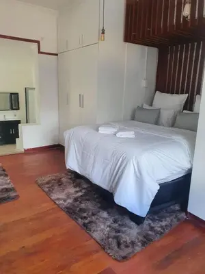 a bedroom with a bed with white sheets and a rug at Ludinz Self Catering Guest House