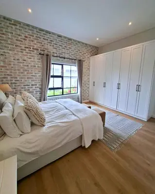 a bedroom with a large bed and a brick wall at Bird's Landing in Hermanus