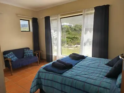 a bedroom with a bed and a couch and a window at Starfish - The rockpool house in Bettyʼs Bay