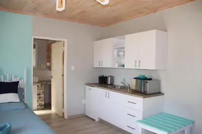 a kitchen with white cabinets and a bed in a room at 7th Heaven Lodge in Gordonʼs Bay