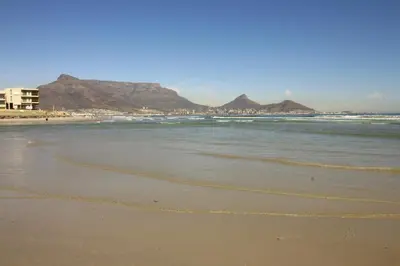 a beach with mountains in the background and the ocean at Westward HO Apartment 13 in Cape Town