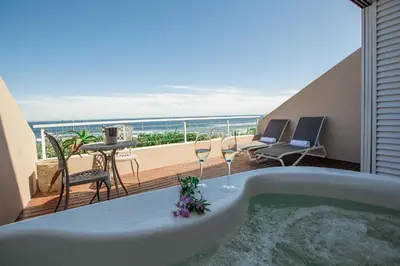 a bath tub with wine glasses and a balcony at Villa Marine Guest House in Pringle Bay
