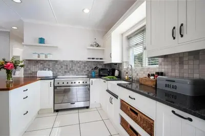 a kitchen with white cabinets and black counter tops at Onrus Cottage in Hermanus