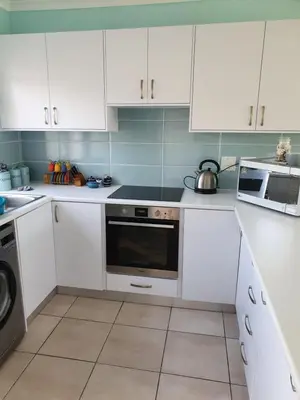 a kitchen with white cabinets and a stove top oven at Sea and Mountain View Apartment in Gordonʼs Bay