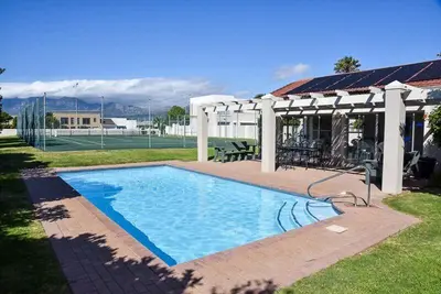 a swimming pool in a yard with a tennis court at Sea and Mountain View Apartment in Gordonʼs Bay