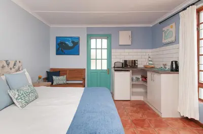 a bedroom with a white bed and a kitchen at 6 Stemmet Lodge in Hermanus