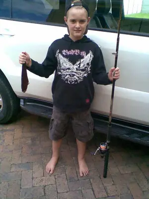 a young boy standing next to a car holding a stick at Kleinmond Panorama Holidays in Kleinmond